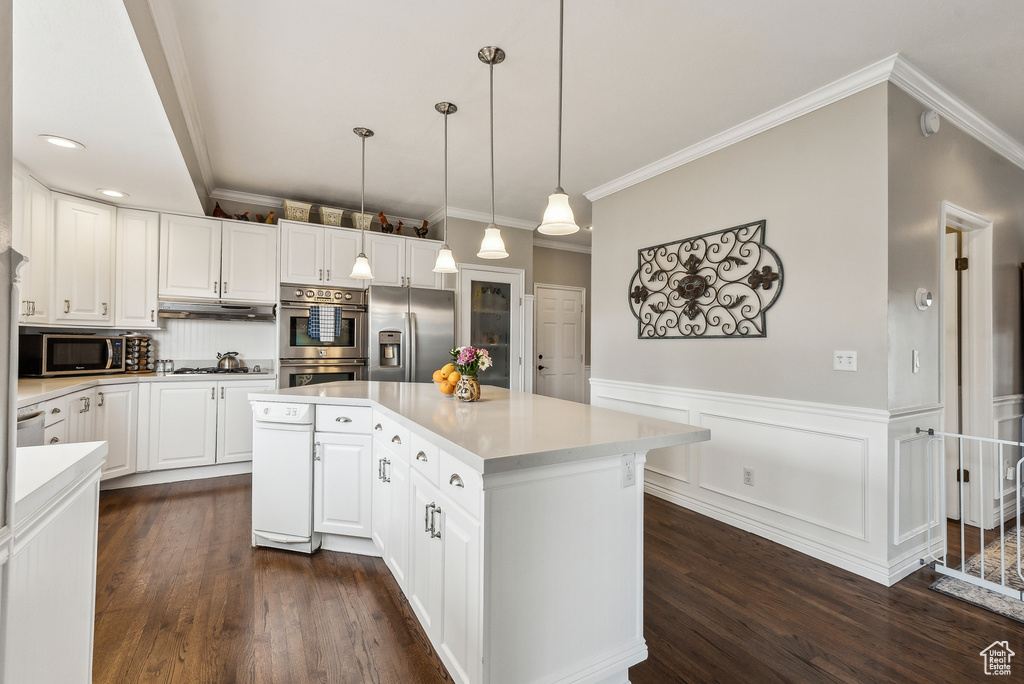 Kitchen with a kitchen island, stainless steel appliances, white cabinets, wainscoting, and light countertops