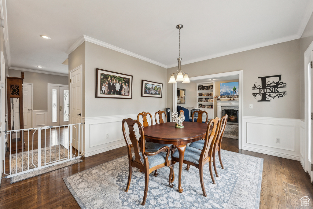 Dining area with built in shelves, wainscoting, recessed lighting, a warm lit fireplace, and wood finished floors