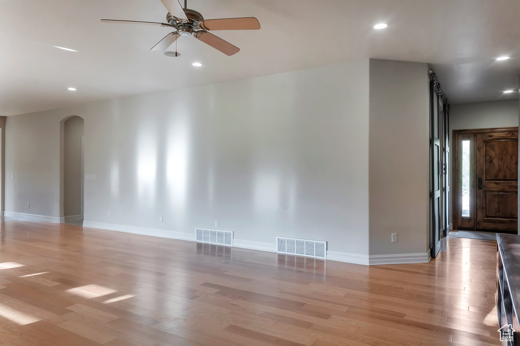 Unfurnished living room featuring arched walkways, light wood-type flooring, a ceiling fan, recessed lighting, and baseboards