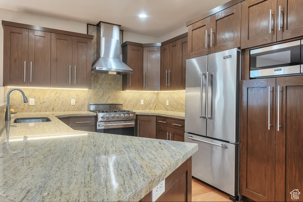 Kitchen with premium appliances, wall chimney range hood, a sink, light stone counters, and recessed lighting