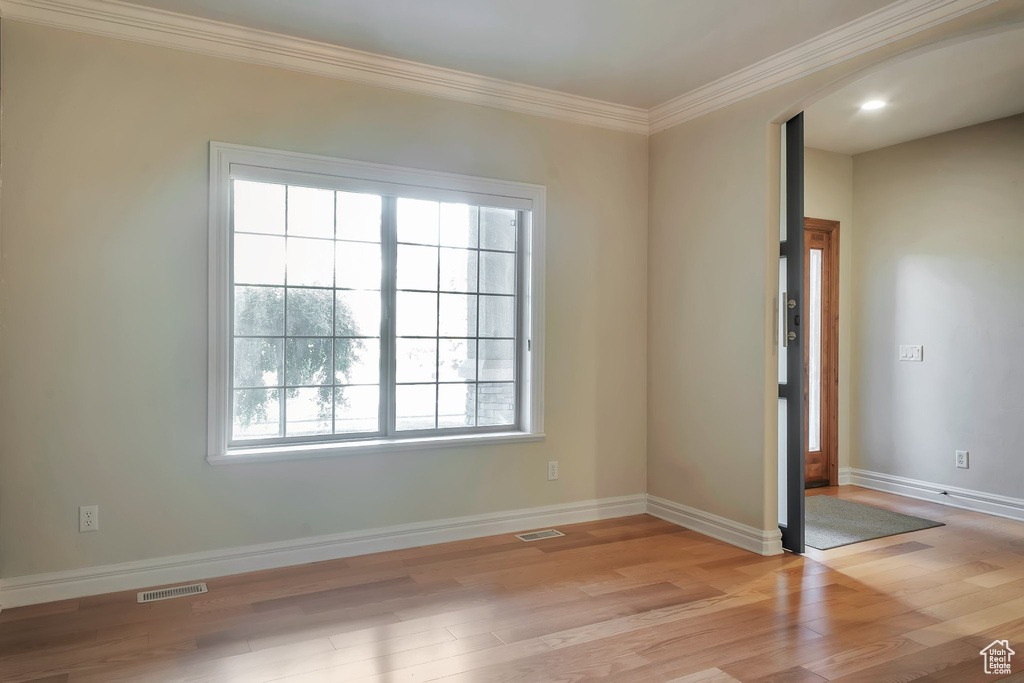 Spare room featuring arched walkways, crown molding, light wood-style floors, and baseboards