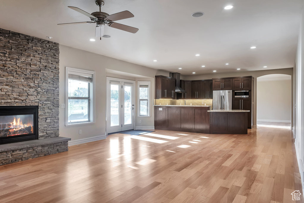 Unfurnished living room with arched walkways, baseboards, recessed lighting, ceiling fan, and a fireplace
