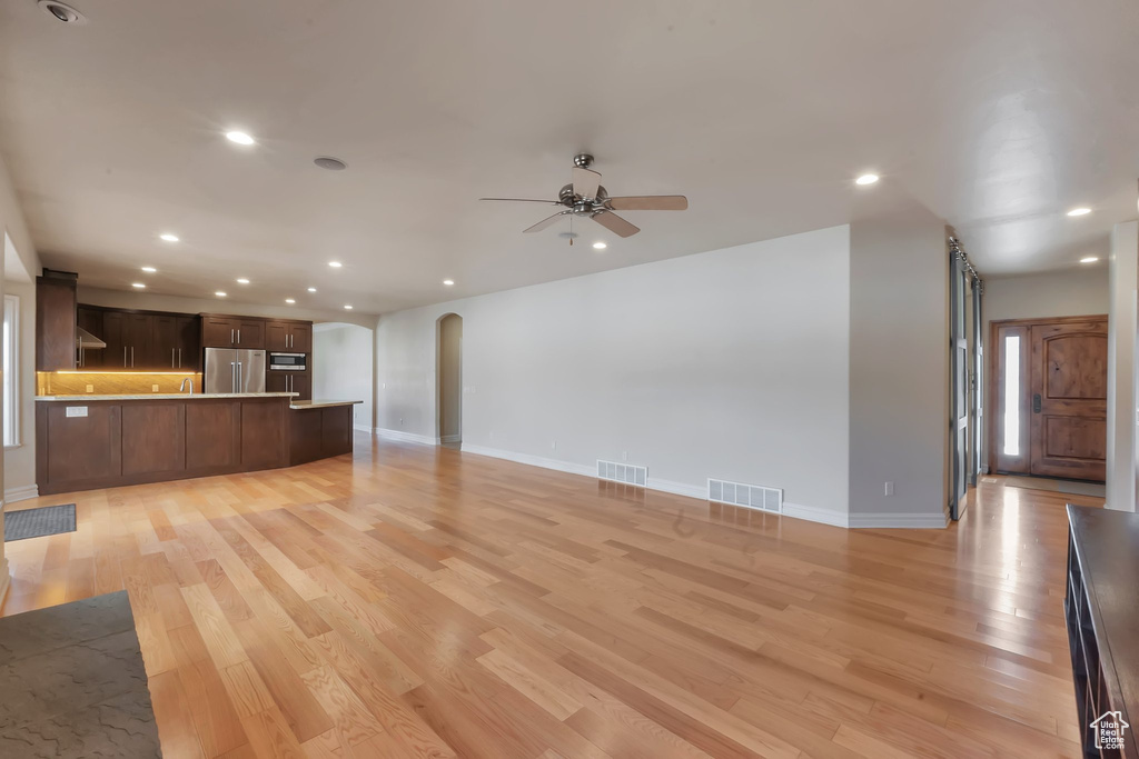 Unfurnished living room featuring arched walkways, recessed lighting, light wood-style floors, a ceiling fan, and baseboards