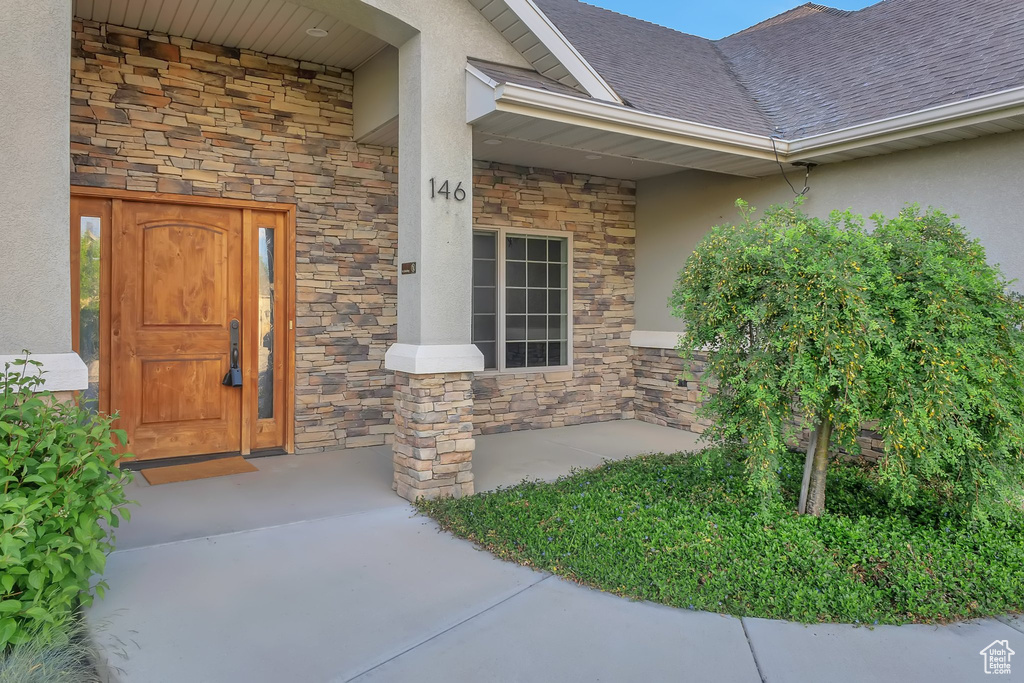 Property entrance with stone siding, stucco siding, roof with shingles, and a porch