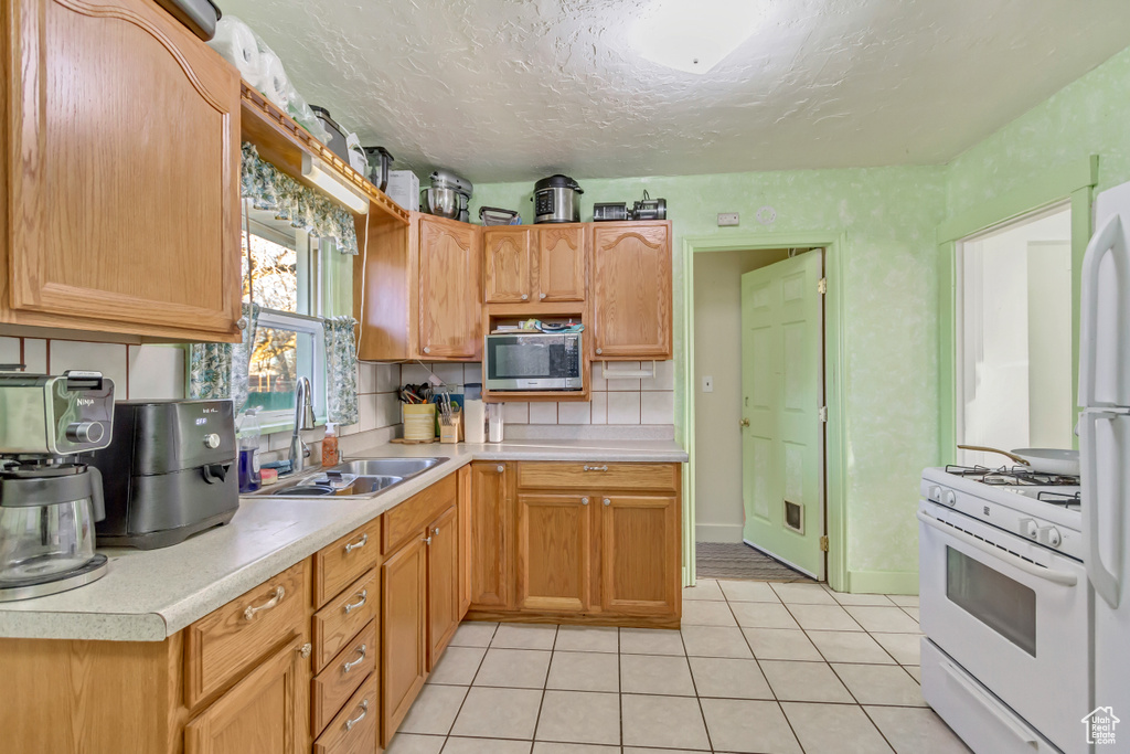 Kitchen with a sink, stainless steel microwave, white gas range oven, light countertops, and light tile patterned floors