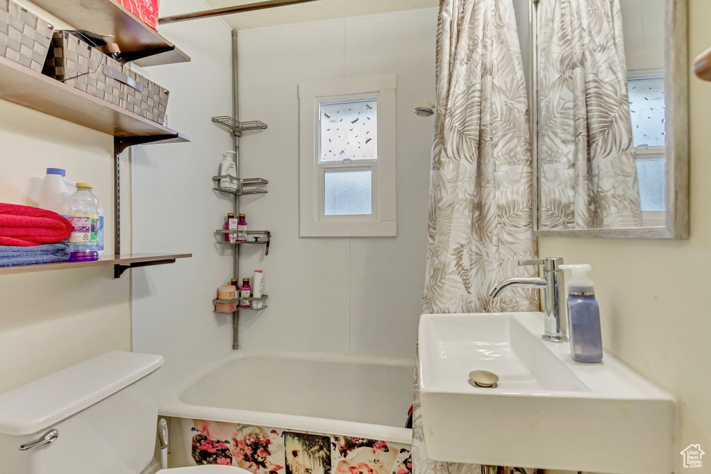 Bathroom featuring toilet, shower / bath combo with shower curtain, and a sink