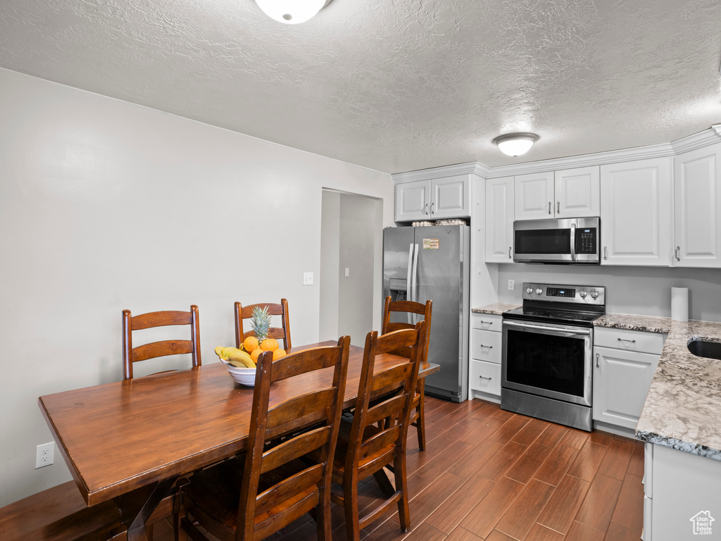 Kitchen featuring light stone countertops, dark wood finished floors, white cabinets, appliances with stainless steel finishes, and a textured ceiling