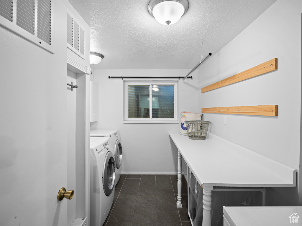 Clothes washing area with visible vents, washer and clothes dryer, cabinet space, a textured ceiling, and dark tile patterned flooring