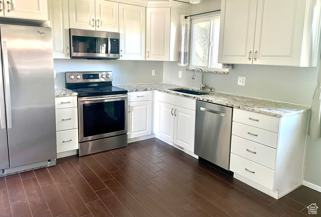 Kitchen featuring dark wood finished floors, appliances with stainless steel finishes, light stone counters, and a sink