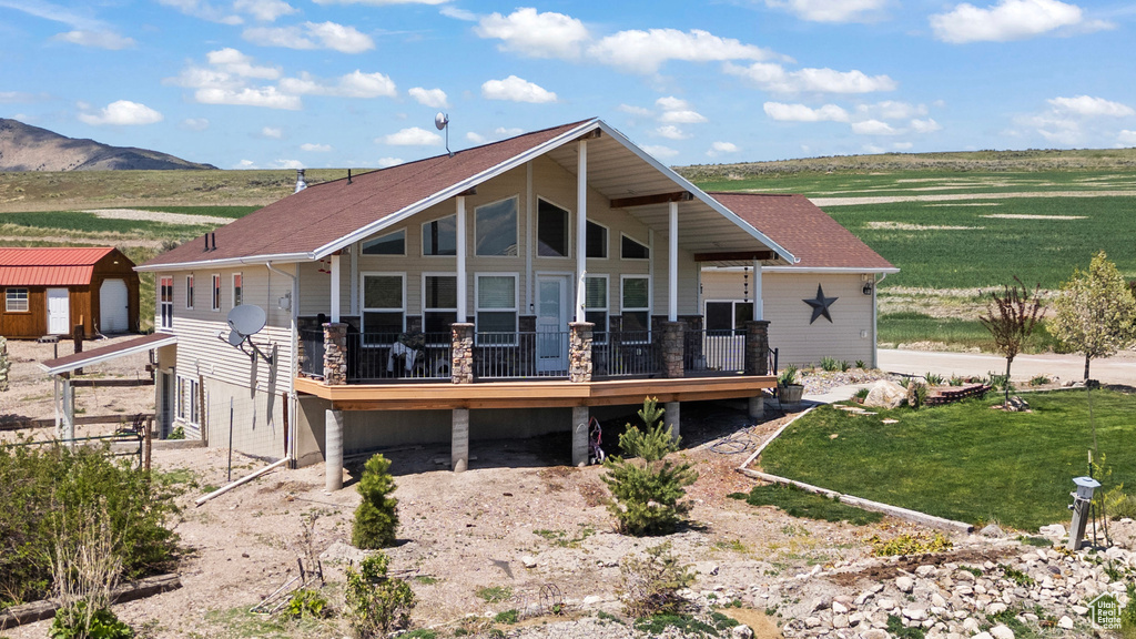 Rear view of property with a deck with mountain view, a yard, an outdoor structure, a storage unit, and stone siding