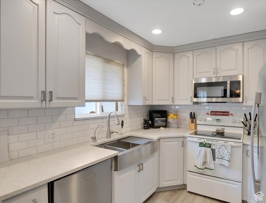 Kitchen featuring tasteful backsplash, white cabinets, stainless steel appliances, and a sink