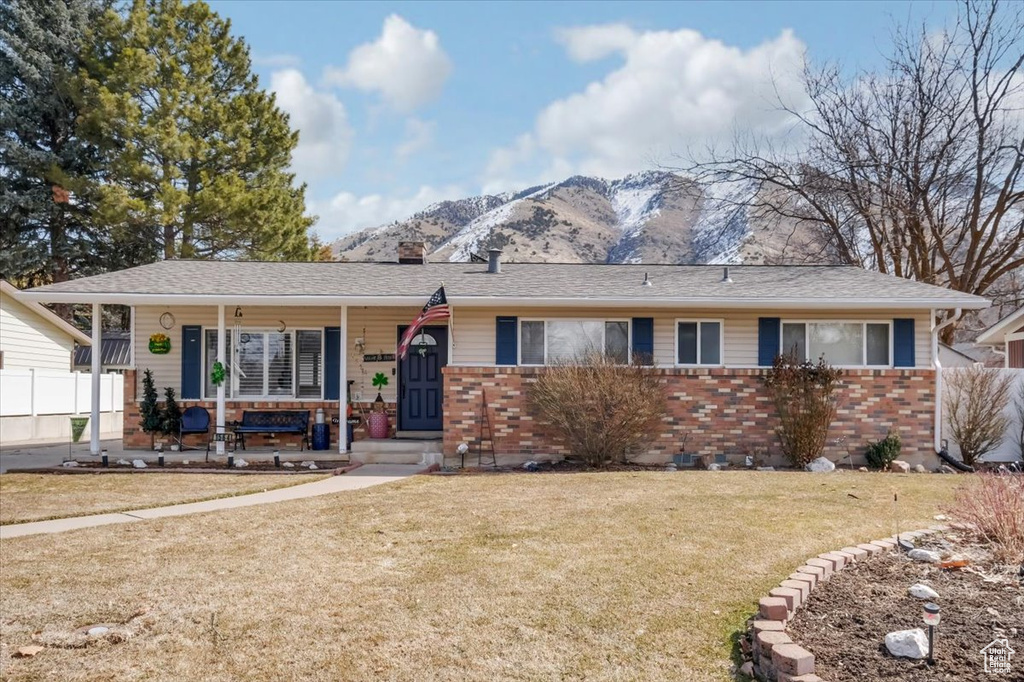 Single story home with brick siding, a front yard, covered porch, a chimney, and a mountain view