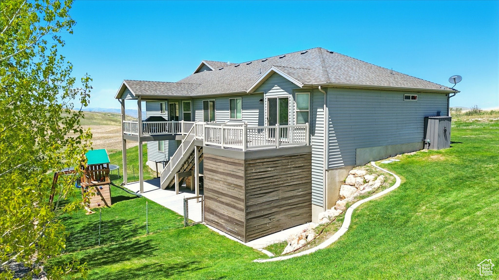 Back of property with a yard, a deck, roof with shingles, and stairway