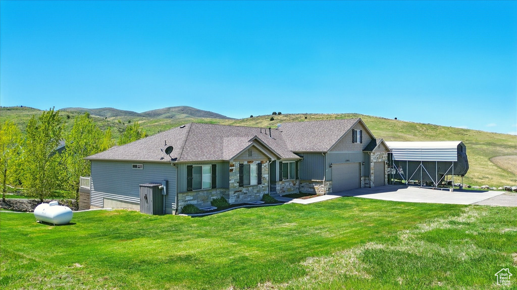 Rear view of property featuring concrete driveway, a lawn, a mountain view, and stone siding