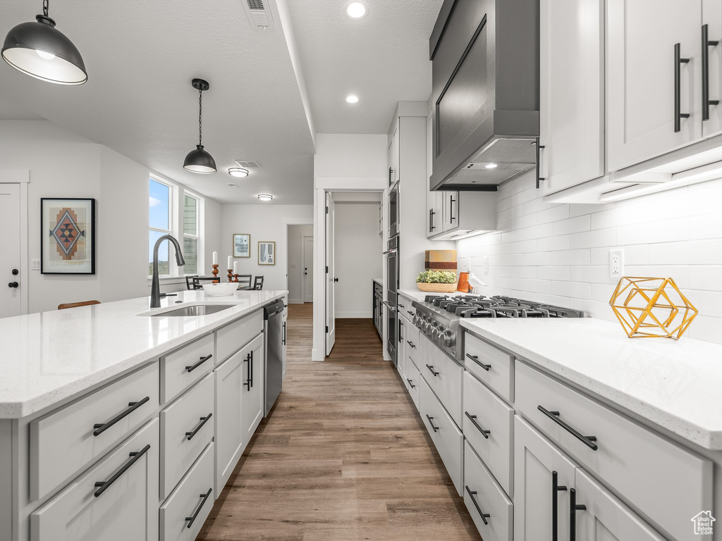 Kitchen featuring a sink, tasteful backsplash, stainless steel appliances, wall chimney exhaust hood, and light wood finished floors