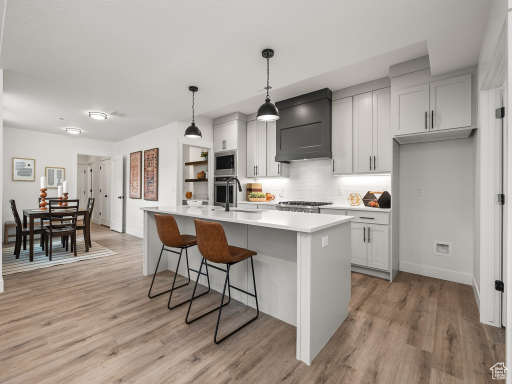 Kitchen with a breakfast bar, a sink, light countertops, custom range hood, and appliances with stainless steel finishes