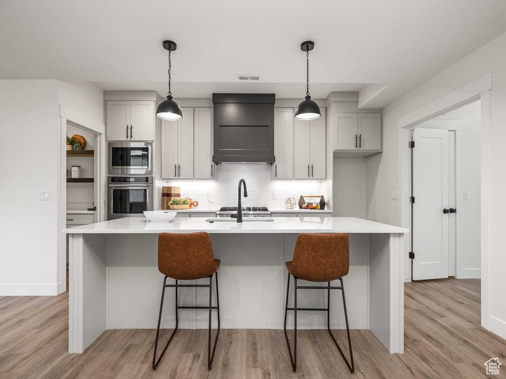 Kitchen featuring visible vents, stainless steel appliances, light countertops, custom range hood, and backsplash