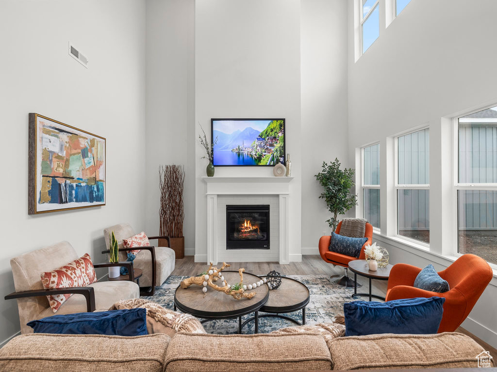 Living area featuring visible vents, a glass covered fireplace, wood finished floors, a high ceiling, and baseboards