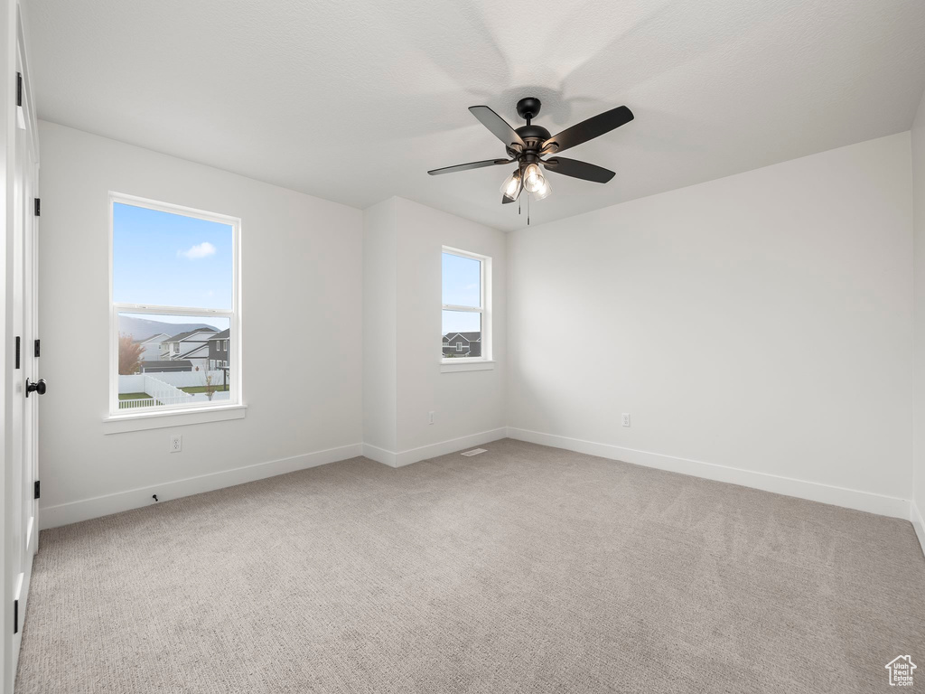 Empty room featuring light carpet, a ceiling fan, and baseboards