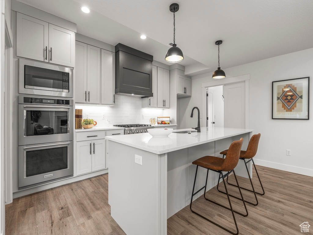 Kitchen featuring light wood-type flooring, a sink, backsplash, stainless steel appliances, and wall chimney exhaust hood