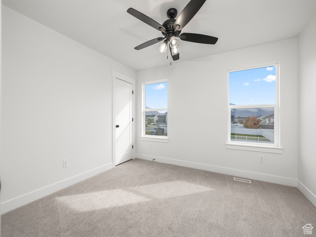 Carpeted empty room featuring plenty of natural light, visible vents, baseboards, and ceiling fan