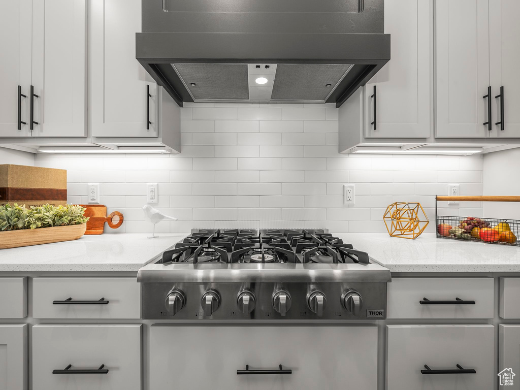 Kitchen with stainless steel gas cooktop, range hood, tasteful backsplash, and light stone countertops