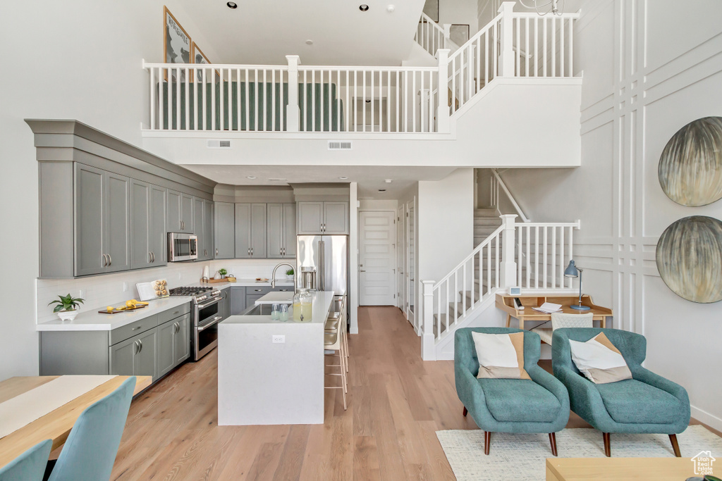 Kitchen featuring light wood-style flooring, gray cabinets, a sink, a towering ceiling, and high quality appliances