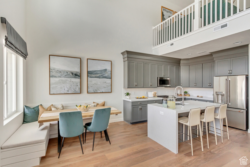 Kitchen with visible vents, gray cabinets, breakfast area, appliances with stainless steel finishes, and a towering ceiling