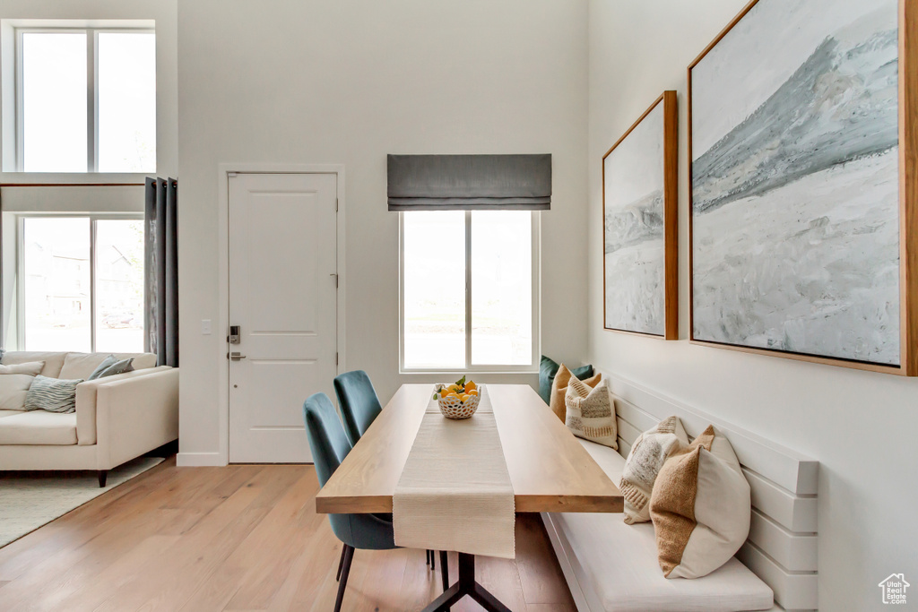 Dining space with baseboards, a healthy amount of sunlight, a towering ceiling, and light wood finished floors