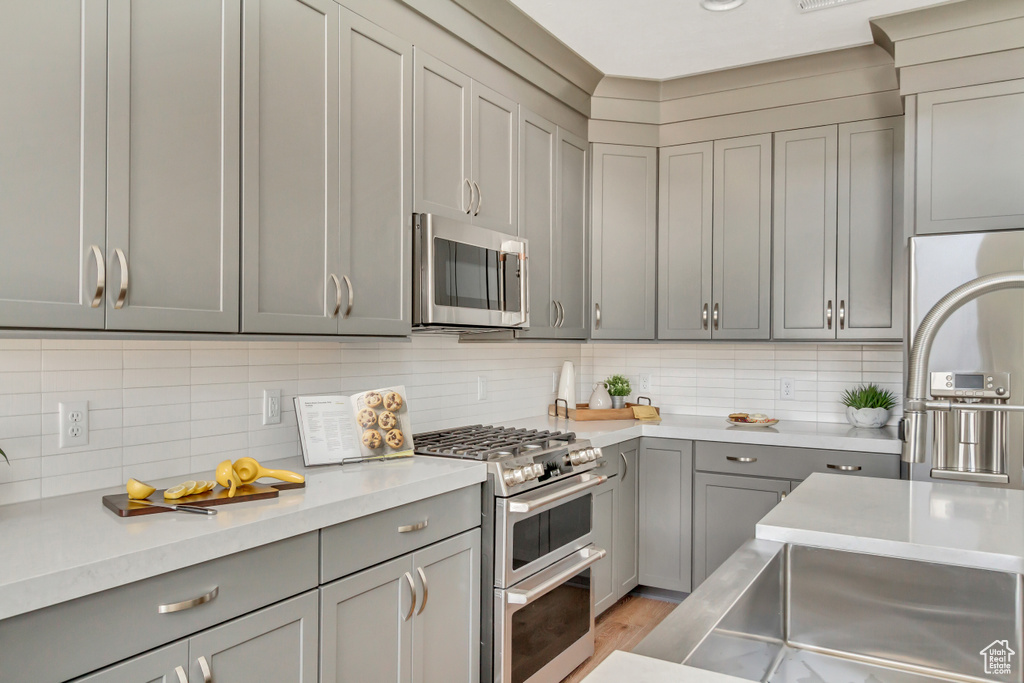 Kitchen with gray cabinetry, light wood-style flooring, stainless steel appliances, light countertops, and decorative backsplash