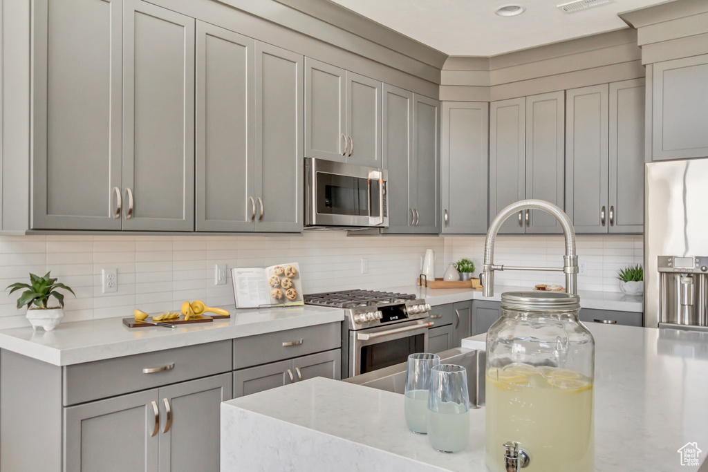 Kitchen featuring visible vents, gray cabinets, a sink, decorative backsplash, and stainless steel appliances