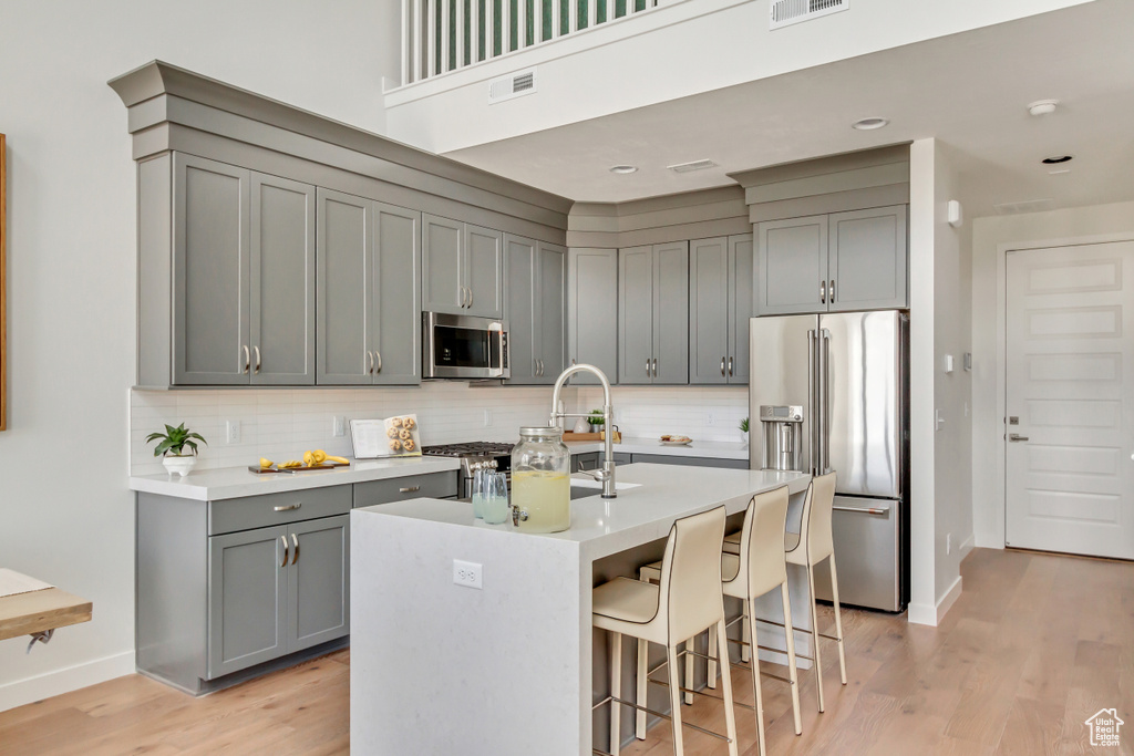 Kitchen with visible vents, gray cabinets, appliances with stainless steel finishes, a breakfast bar area, and decorative backsplash