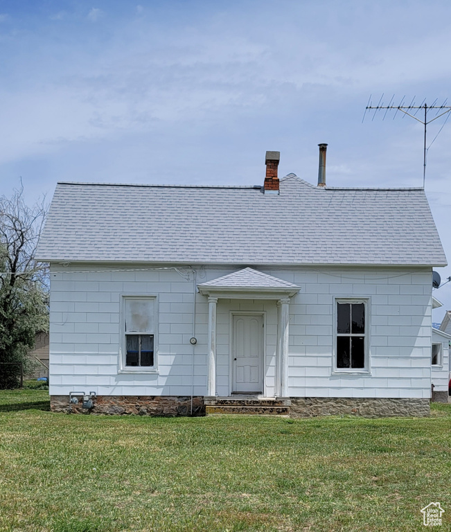 View of front of home featuring a front lawn, roof with shingles, and a chimney