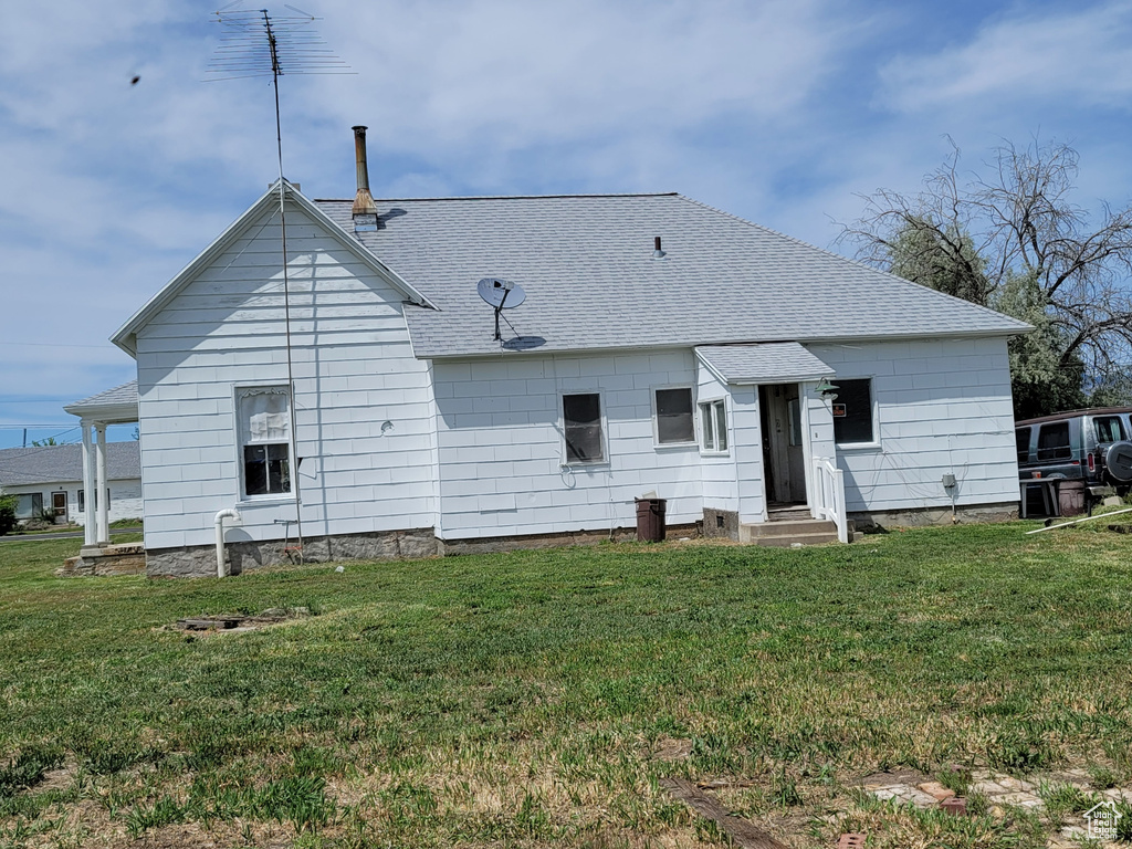Back of house with a shingled roof, entry steps, and a yard