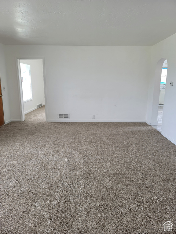 Unfurnished room featuring arched walkways, light colored carpet, and healthy amount of natural light