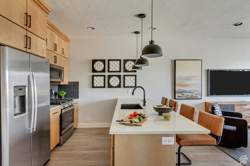 Kitchen featuring light brown cabinets, a sink, stainless steel appliances, light wood-style floors, and light countertops