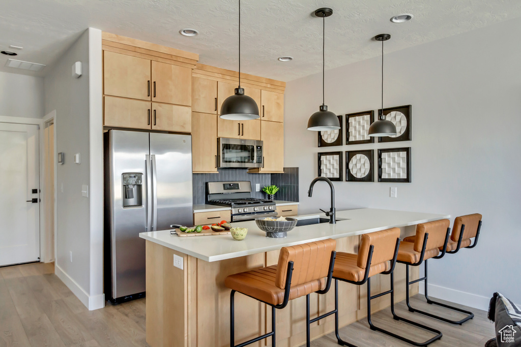 Kitchen featuring light wood finished floors, backsplash, light brown cabinetry, a peninsula, and stainless steel appliances