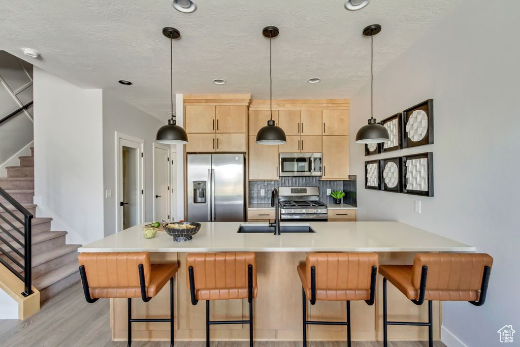 Kitchen featuring light brown cabinetry, a sink, backsplash, stainless steel appliances, and a breakfast bar area