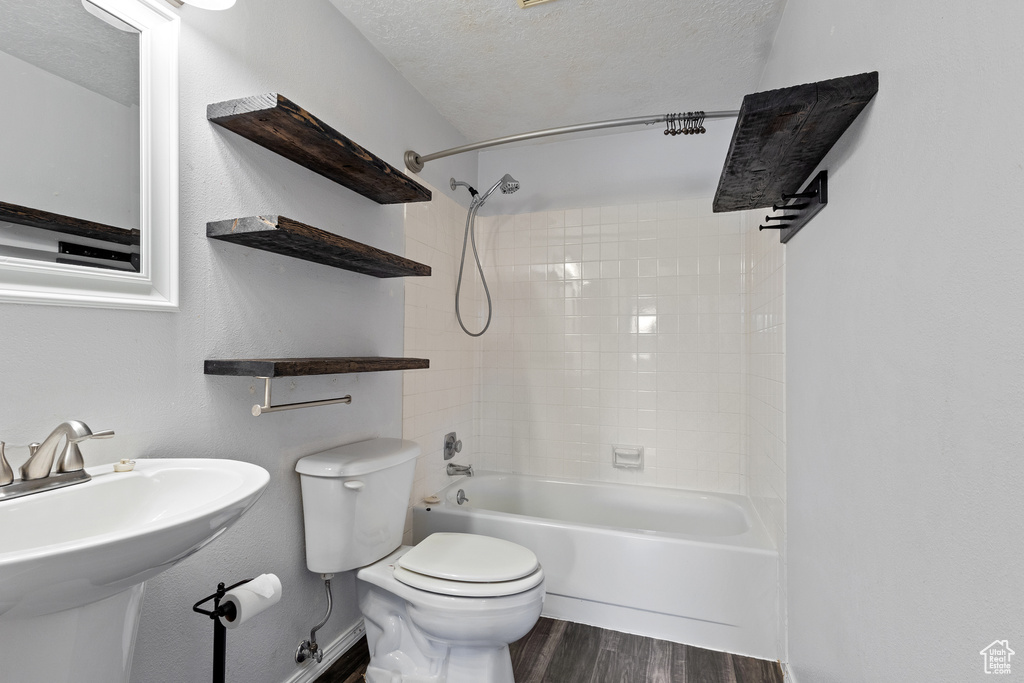 Bathroom with wood finished floors, toilet, a textured ceiling, shower / bathing tub combination, and a sink