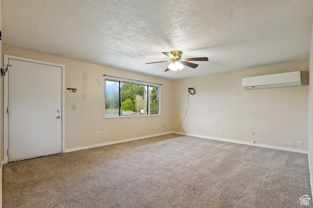 Carpeted empty room featuring baseboards, a ceiling fan, a textured ceiling, and a wall unit AC