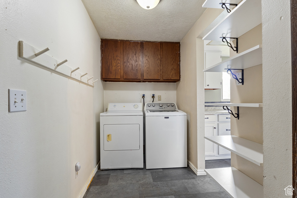 Clothes washing area with a textured ceiling, cabinet space, and washer and dryer