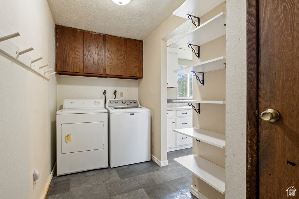Laundry room featuring a textured ceiling, baseboards, washing machine and dryer, and cabinet space