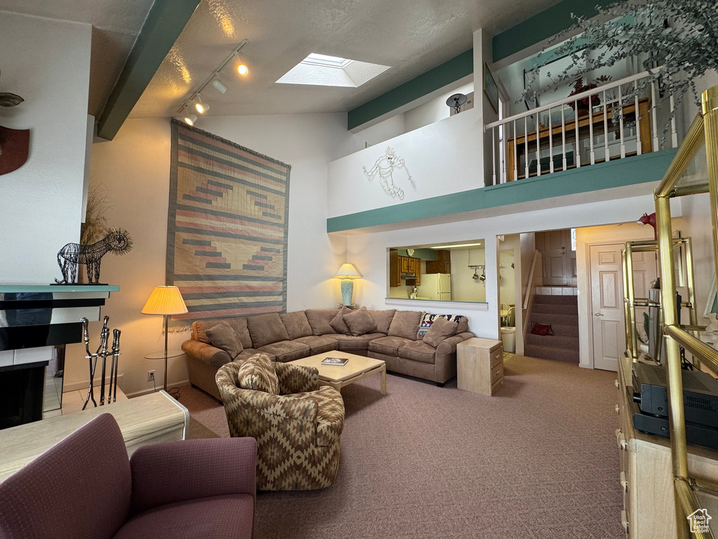 Carpeted living room with stairway, a skylight, and high vaulted ceiling
