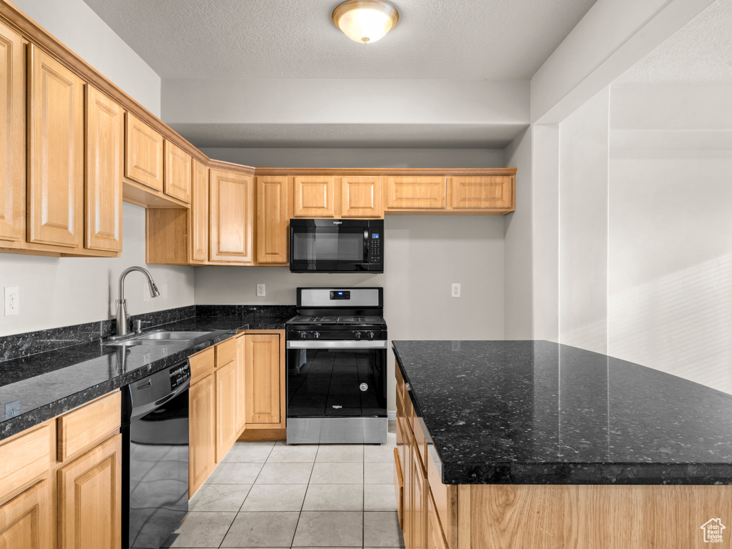 Kitchen featuring a sink, a textured ceiling, a center island, light tile patterned floors, and black appliances