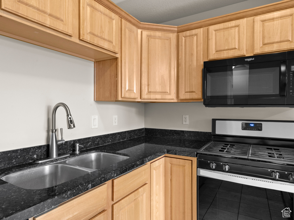Kitchen featuring light brown cabinets, a sink, black microwave, stainless steel gas stove, and tile patterned flooring