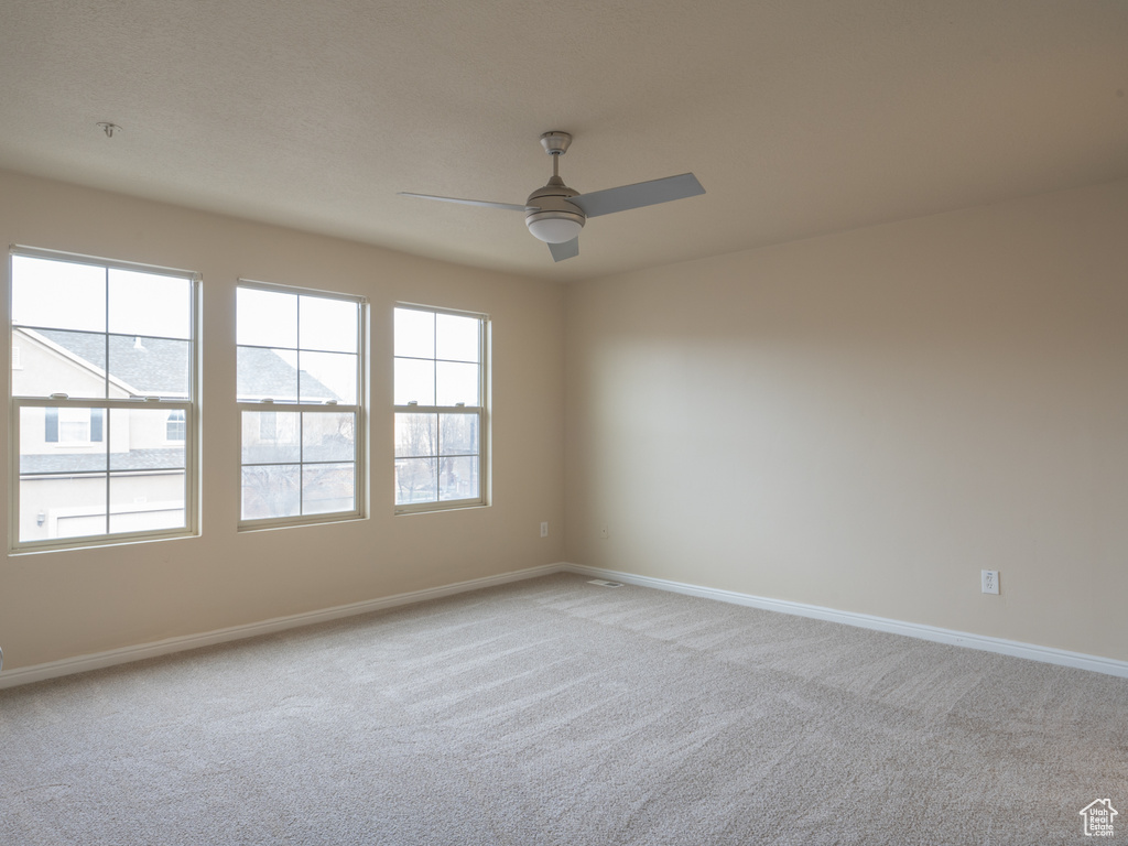 Carpeted empty room featuring baseboards and a ceiling fan