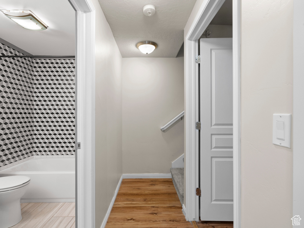 Full bath featuring a textured ceiling, baseboards, wood finished floors, toilet, and shower / washtub combination