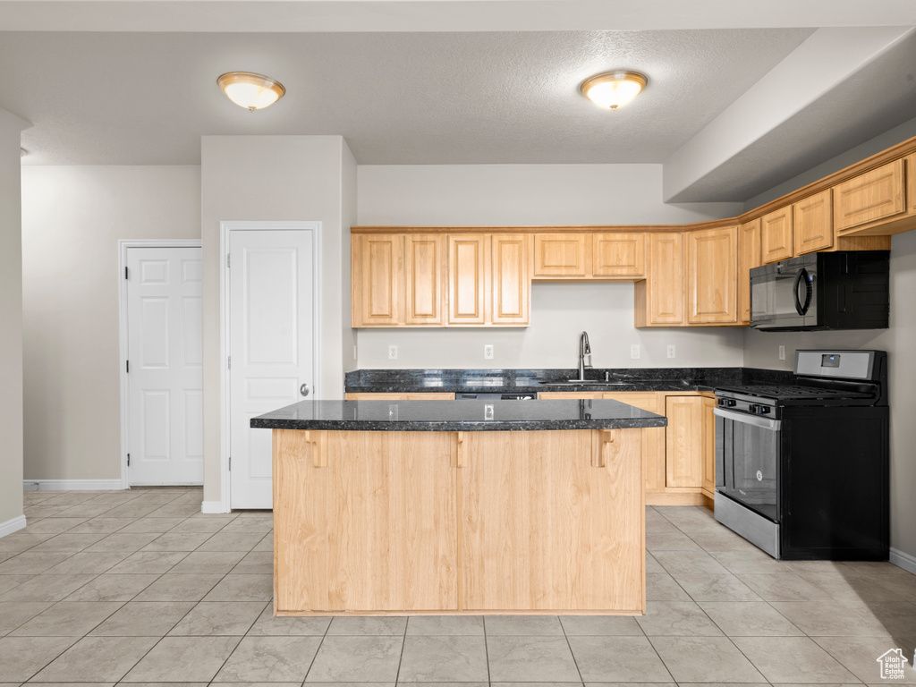 Kitchen with a sink, black microwave, a center island, dark stone countertops, and gas stove