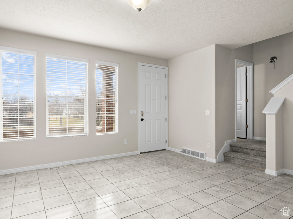 Foyer with a textured ceiling, visible vents, baseboards, stairway, and light tile patterned floors