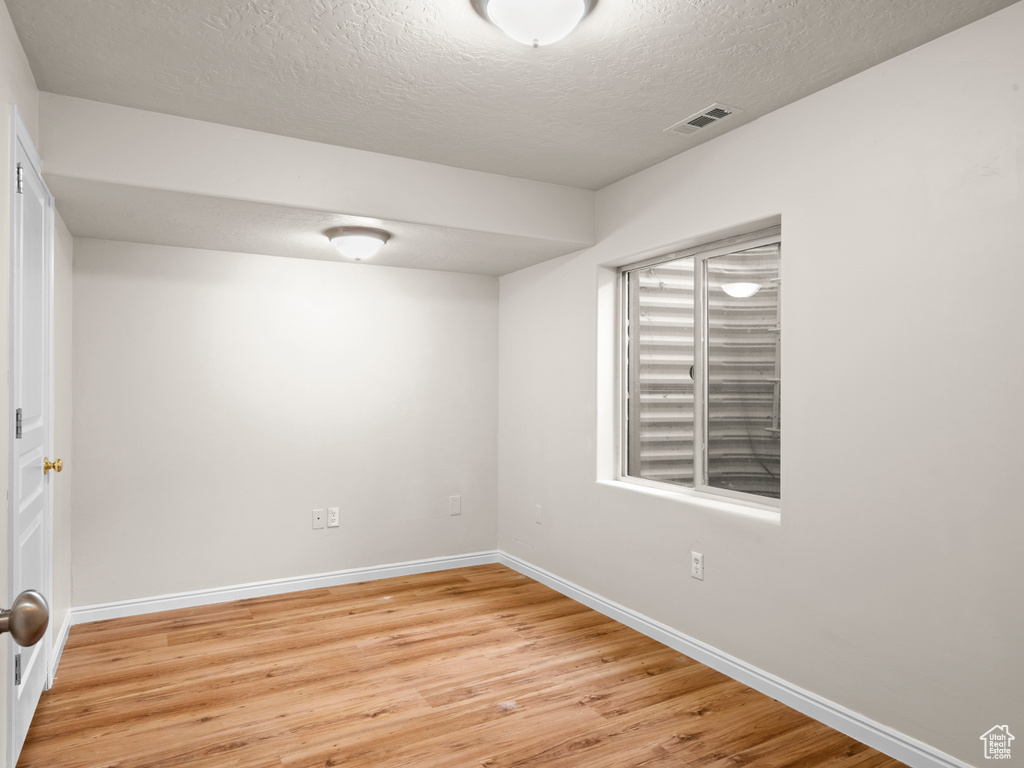 Spare room with baseboards, light wood-type flooring, visible vents, and a textured ceiling